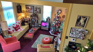 Ein gemütliches Wohnzimmer mit Sofa, Sessel und Couchtisch, einem Fernseher, einem Weihnachtsbaum sowie einer Wand mit Fotos und einer Uhr.