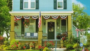Ein zweistöckiges Haus mit Veranda, einem kleinen Garten mit Blumen und einer Flagge.