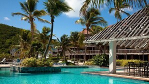 Ein Hotelpool mit Palmen, einer überdachten Sitzgelegenheit und einem Gebäude mit einem Ziegeldach.