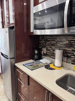 A kitchen with a stainless steel refrigerator, a microwave, a coffee maker, and a sink.
