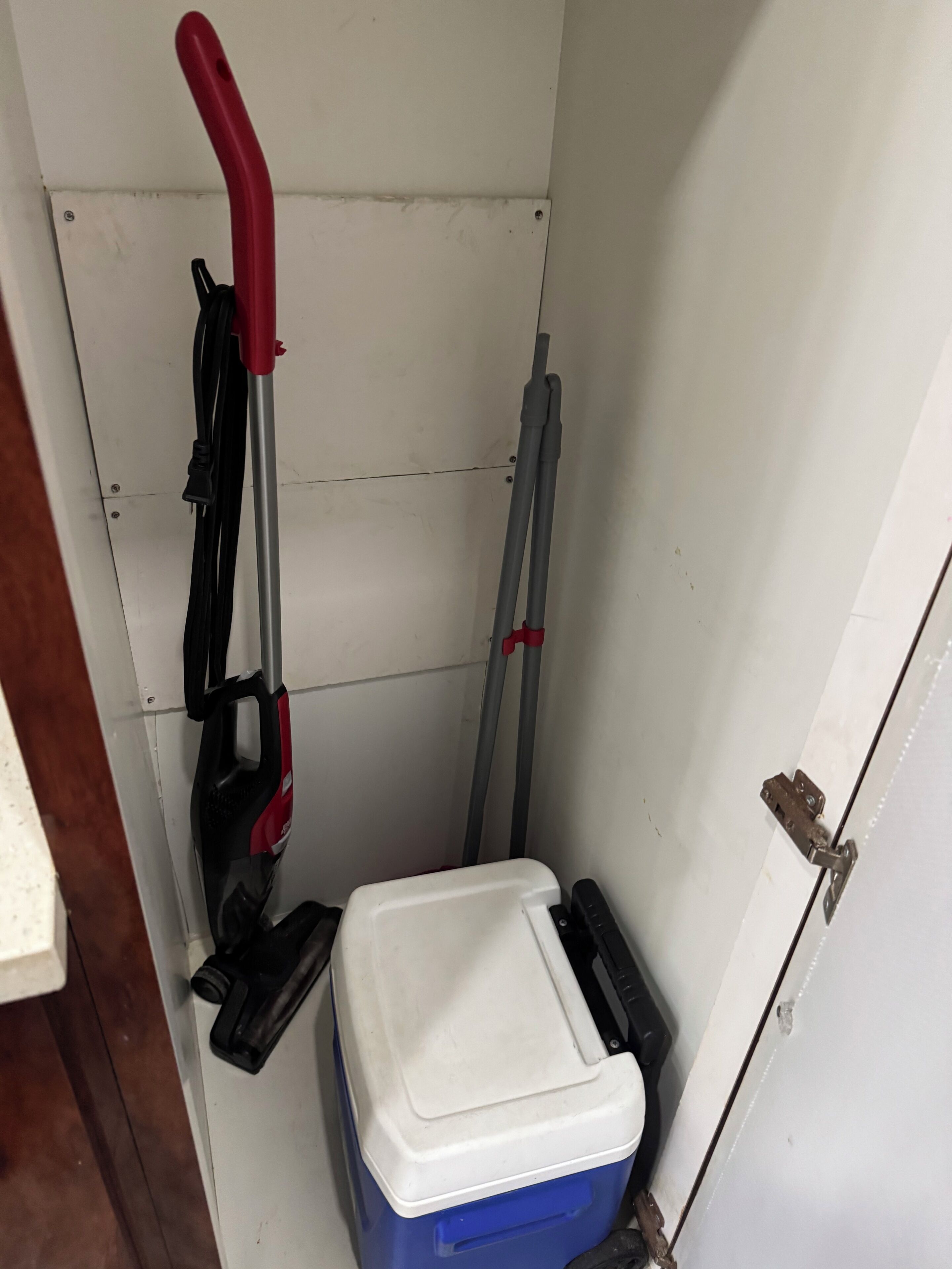 A small room with a white door, a blue cooler, and a red and black vacuum cleaner.