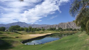 Um campo de golfe com lago, colinas verdes e montanhas ao fundo.