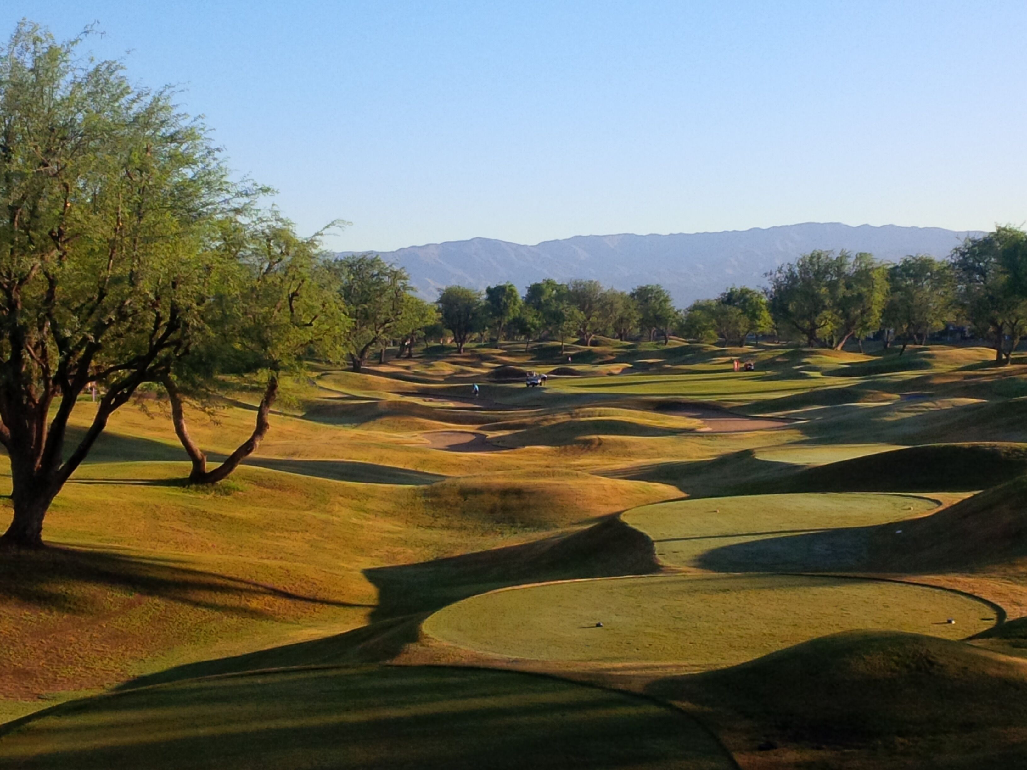 A golf course with rolling hills, trees, and distant mountains.