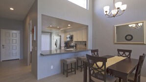 Cozinha moderna com ilha central, banquetas e mesa de jantar com cadeiras.