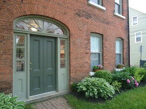 A brick building with a green door, two windows, and a small garden with plants and flowers.
