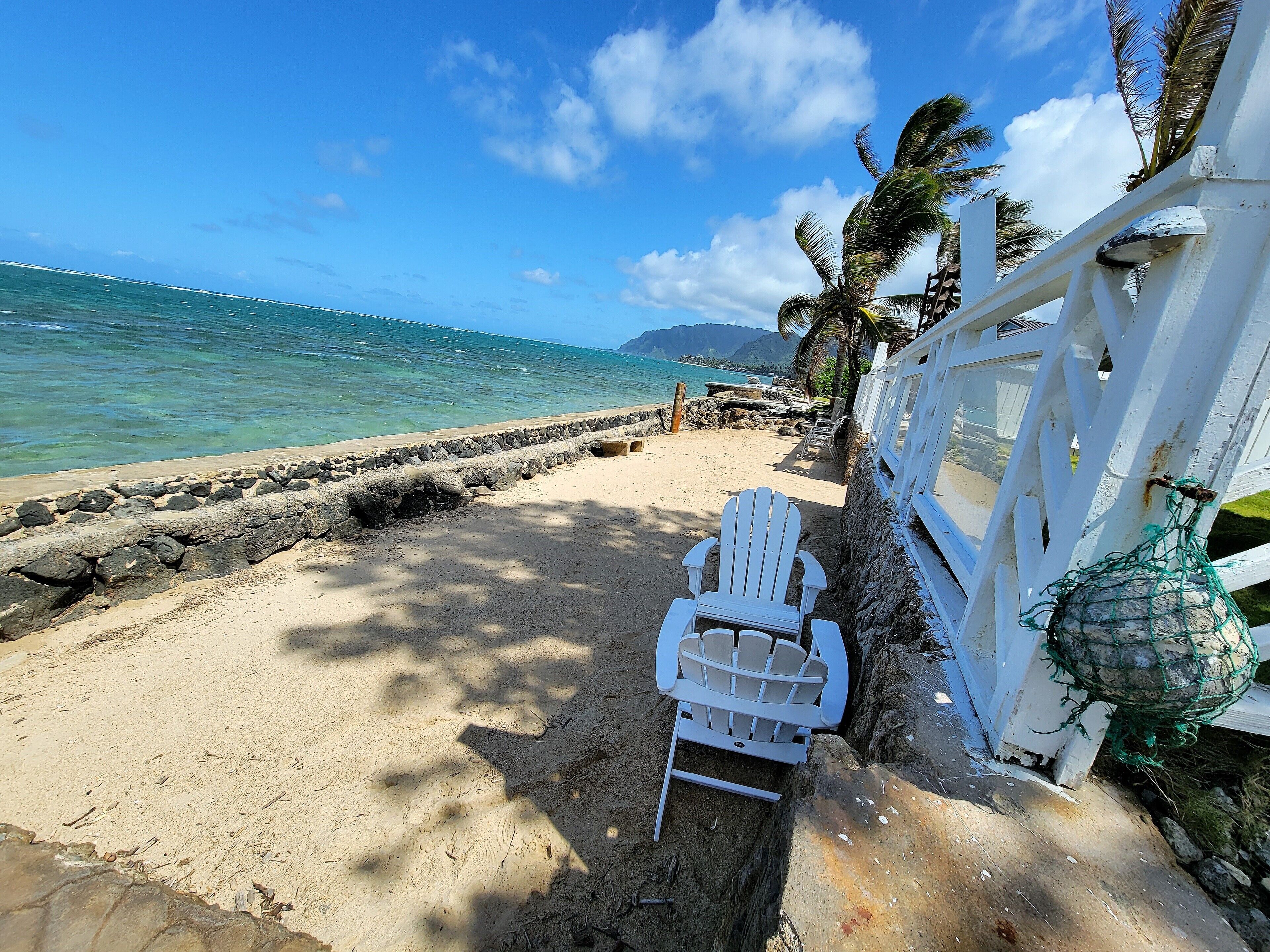 A beach with a white fence, a white chair, and a rocky shoreline.
