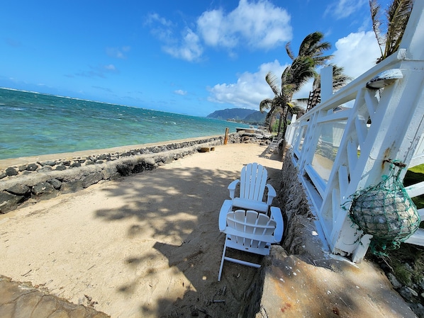 A beach with a white fence, a white chair, and a rocky shoreline.