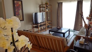 Una sala de estar con un sofá de madera, un televisor sobre un mueble de madera, una mesa de centro y un jarrón con flores.