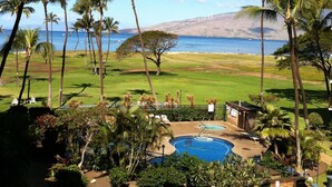 A pool area with a view of the ocean, surrounded by palm trees and a grassy landscape. - Kauhale Makai: 1 Bedroom with Ocean Views, Fully Remodeled and Redecorated (Kihei, Maui)