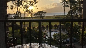 A balcony with a view of the ocean and palm trees at sunset. - Kauhale Makai: 1 Bedroom with Ocean Views, Fully Remodeled and Redecorated (Kihei, Maui)