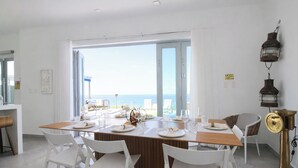 A modern dining area with a wooden table, white chairs, and a view of the sea. - Luxury Ocean Front Villa with Heated Infinity Pool, Private Pier and Kayaks (Cabo Rojo)