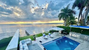 A pool area with lounge chairs and a barbecue, overlooking the ocean. - Luxury Ocean Front Villa with Heated Infinity Pool, Private Pier and Kayaks (Cabo Rojo)