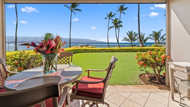 Eine Terrasse mit Tisch und Stühlen, einem Blumenstrauß und Blick auf das Meer und Palmen.