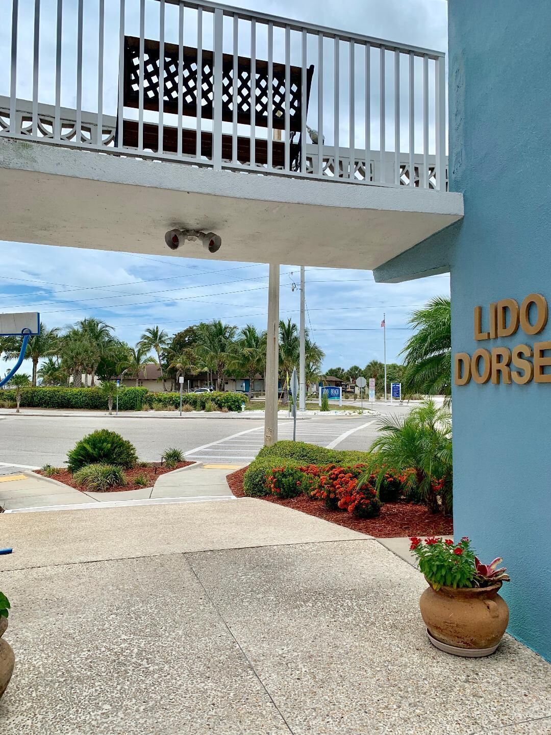 Entrada de hotel con un paseo techado, palmeras y un letrero que dice "LIDO DORSE".