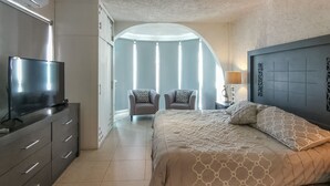 A modern bedroom with a large bed, a TV on a cabinet, and a chair with a view of the outside.