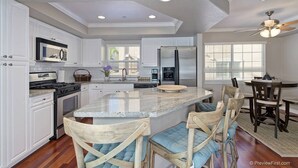 Una cocina moderna con armarios blancos, una isla central, taburetes de bar y un ventilador de techo.