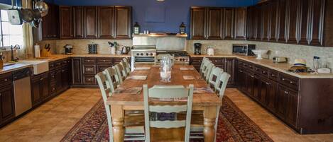 A spacious kitchen with dark wooden cabinets, a large dining table, and a patterned rug.