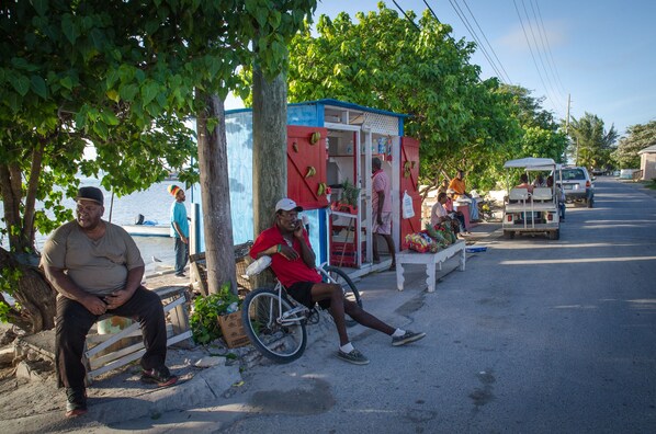 A roadside stall with a blue and red exterior, a bicycle, and a man sitting on a bench. - Seadream House – Large 5-Bedroom Oceanview Retreat (Dunmore Town)