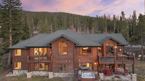 A two-story log cabin with a stone foundation, large windows, and a hot tub in the front yard. - Moosehead Lodge: Clear Mountain Views, Hot Tub & Game Room (Breckenridge)