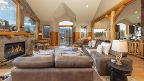 A spacious living room with a stone fireplace, a large sofa, and a dining area with a view of the mountains. - Moosehead Lodge: Clear Mountain Views, Hot Tub & Game Room (Breckenridge)