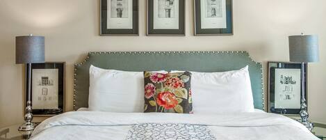 A neatly made bed with a patterned bedspread, a decorative pillow, and a headboard with a beaded trim. There are three framed pictures on the wall above the bed.