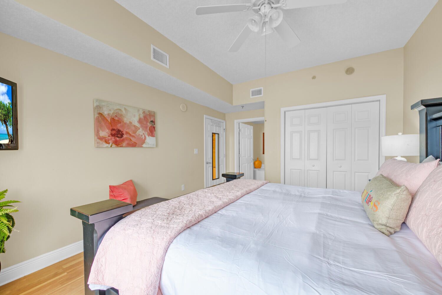 A bedroom with a large bed, a nightstand, a ceiling fan, and a door leading to another room.