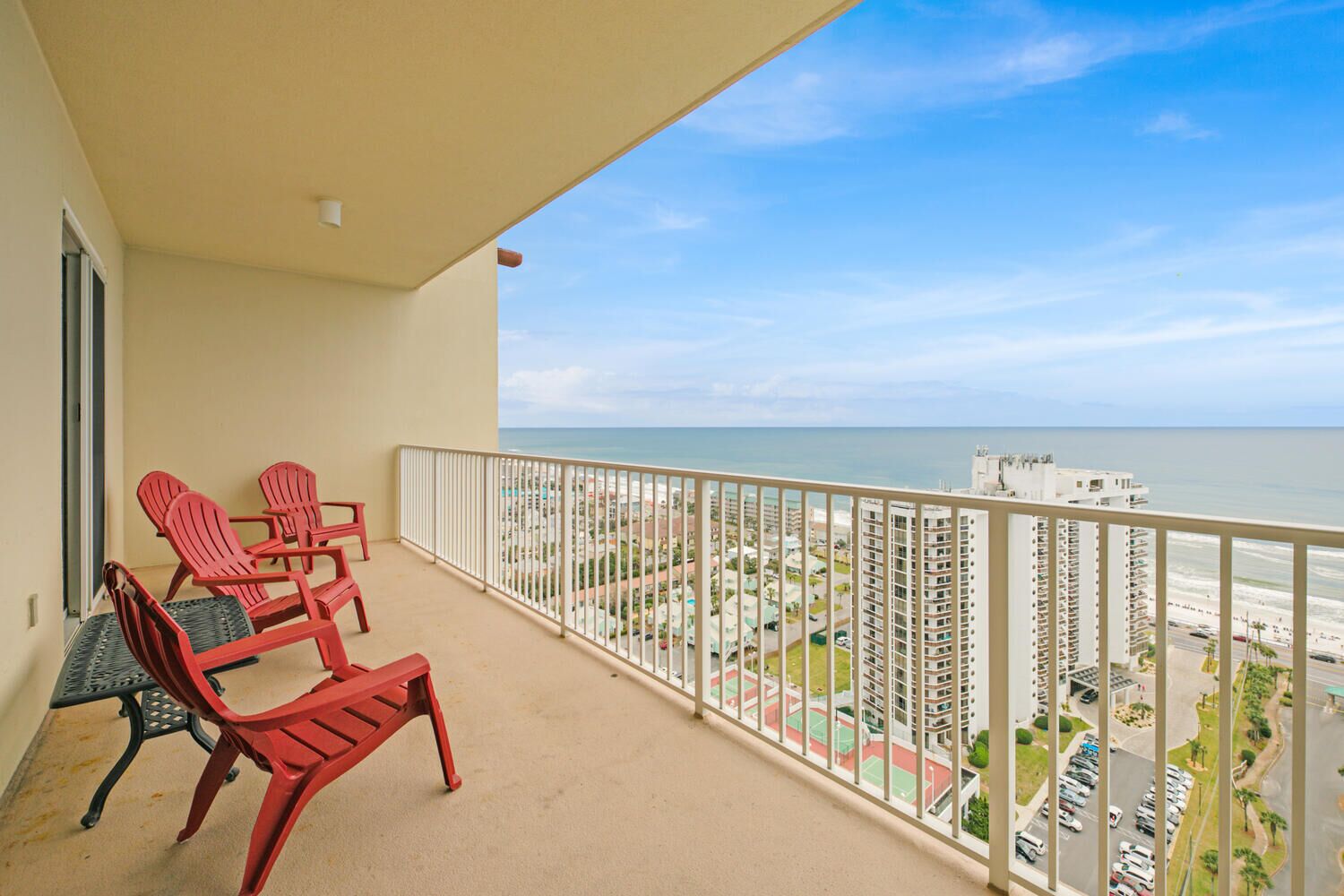 A balcony with red chairs and a view of the beach and buildings.