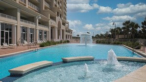 A swimming pool with a fountain, surrounded by lounge chairs and a hotel building with balconies. - Ariel Dunes - Amazing Gulf Views, Pools, Gym, Walk to Beach, On-Site Dining.  😎 (Miramar Beach)