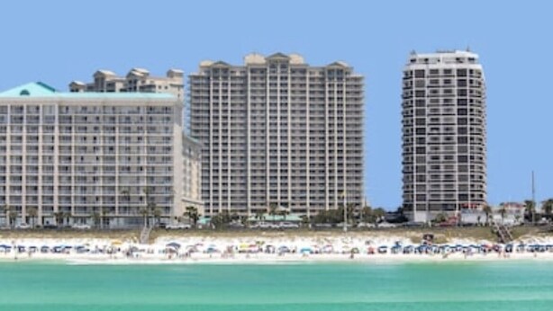 A beachfront hotel with multiple high-rise buildings, a sandy beach, and a clear blue sky. - Ariel Dunes - Amazing Gulf Views, Pools, Gym, Walk to Beach, On-Site Dining.  😎 (Miramar Beach)