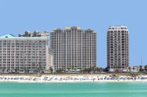 A beachfront hotel with multiple high-rise buildings, a sandy beach, and a clear blue sky.