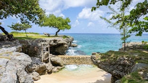 A natural beach setting with clear turquoise water, rocky formations, and lush greenery.
