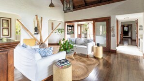 A spacious living area with a white sofa, a coffee table, and a large woven rug. There are wooden beams on the ceiling and a hanging lantern.