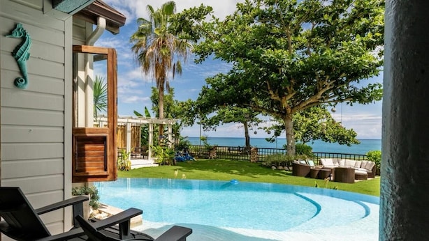 A swimming pool with a view of the ocean, a wooden deck, and outdoor furniture.