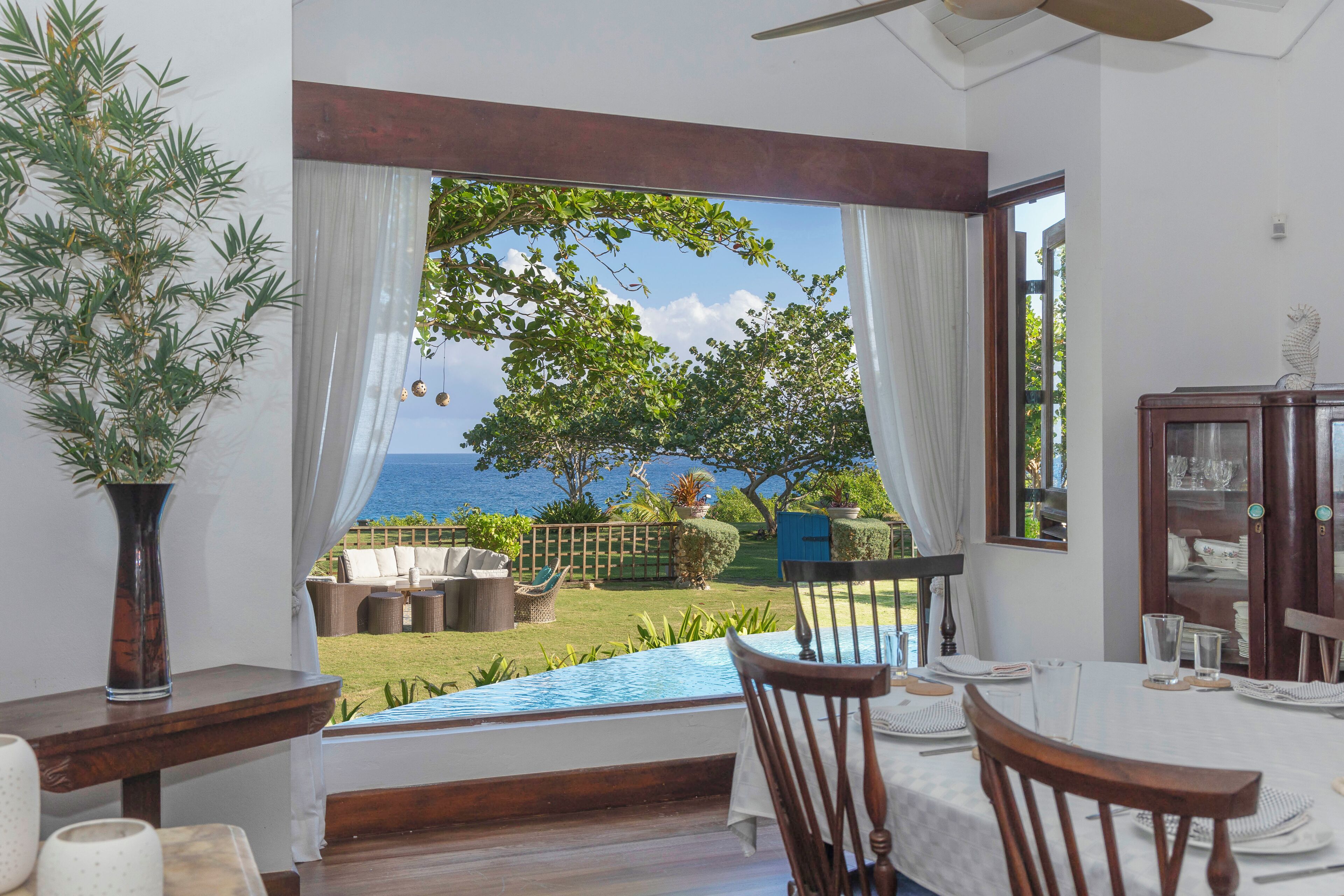 A dining area with a view of the sea, a wooden table, chairs, and a vase of flowers.