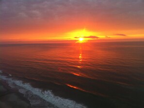 A sunset over the ocean with waves approaching the shore.