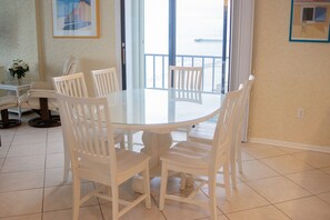 A dining area with a round glass table surrounded by white chairs, a white cabinet, and a potted plant.