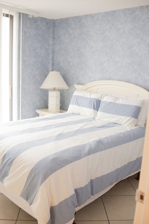 A bedroom with a bed, a nightstand, a lamp, and a window.