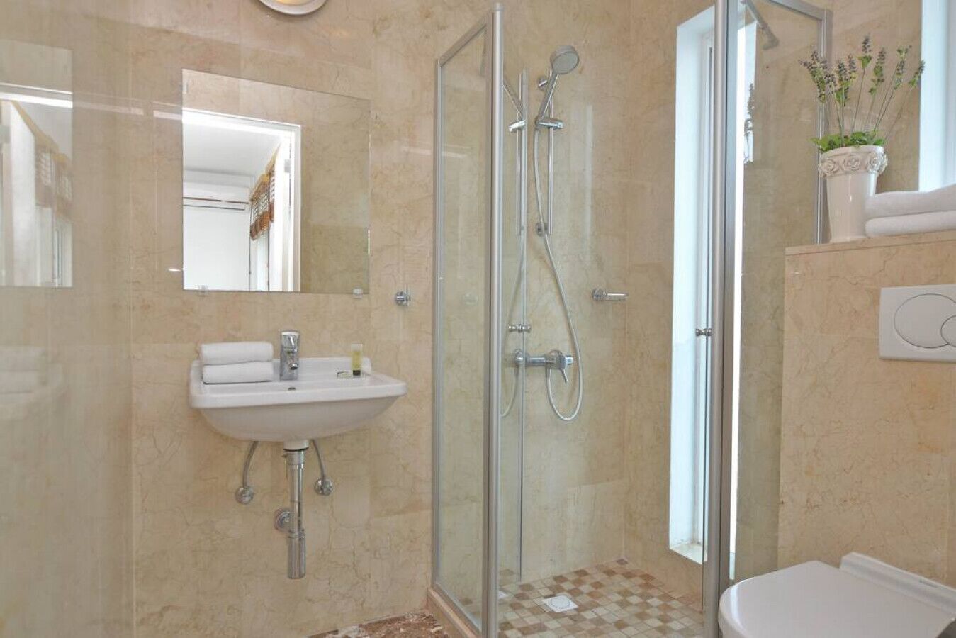 Ein modernes Badezimmer mit einer gläsernen Dusche, einem Waschbecken mit Spiegel und einer Topfpflanze.
