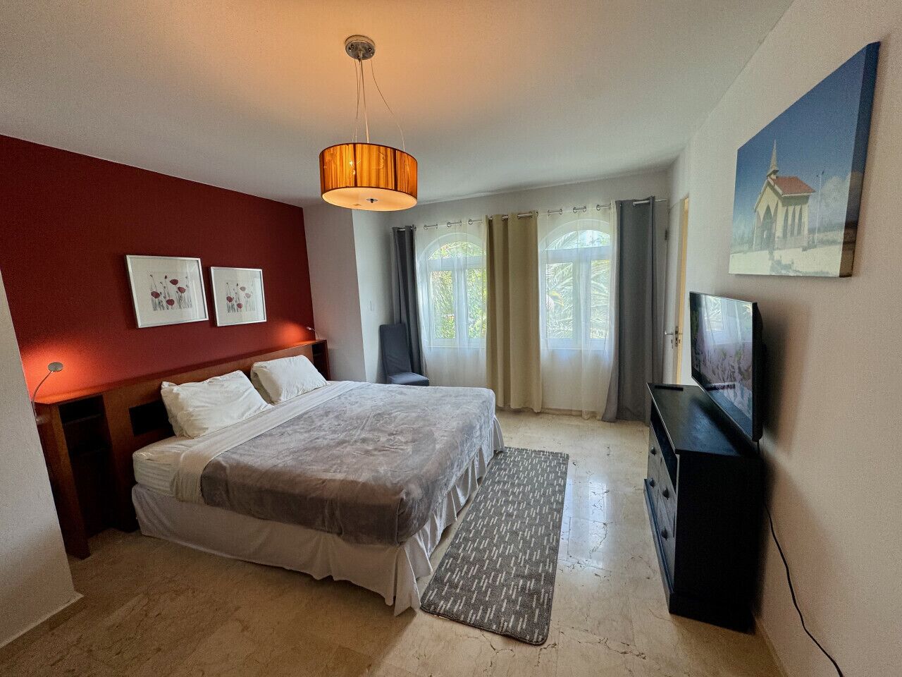 A bedroom with a bed, a television, a desk, and a window with curtains.