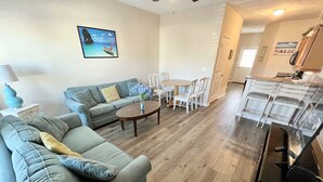 A modern living room with a sectional sofa, a coffee table, and a dining area with white chairs. - 343 Sailors, Beautiful 2-bedroom cottage in Myrtle Beach, 2 Blocks to the Beach! (Myrtle Beach)