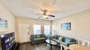 A living room with a ceiling fan, a television, a sofa, a coffee table, and a dining table with chairs. - 343 Sailors, Beautiful 2-bedroom cottage in Myrtle Beach, 2 Blocks to the Beach! (Myrtle Beach)