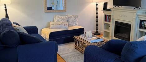 A living room with two blue sofas, a coffee table, a fireplace, a TV, and a bookshelf.