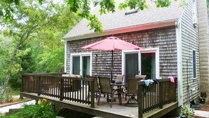 A wooden deck with outdoor furniture and a red umbrella. - Highly Rated Cottage in Orleans, Cape Cod (Orleans)
