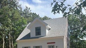 A two-story house with a gabled roof, a front porch with a brick pathway, and a small garden with flowers. - Highly Rated Cottage in Orleans, Cape Cod (Orleans)