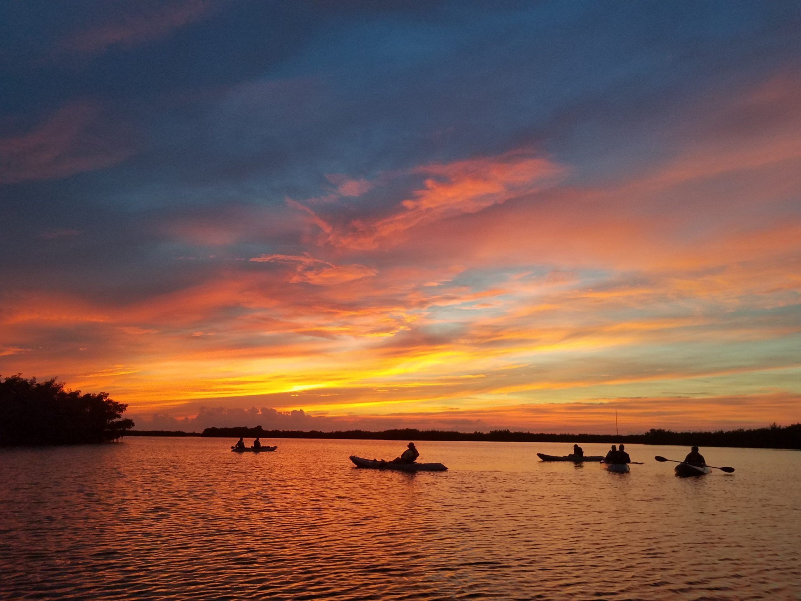 Un coucher de soleil sur une étendue d’eau calme, avec plusieurs kayaks.