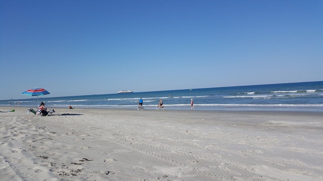 A beach with a clear sky, a few people, and a ship in the distance.