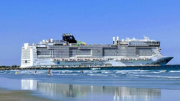 Ein großes Kreuzfahrtschiff liegt an einem Strand bei strahlendem Himmel.