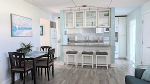 Eine moderne Küche mit weißen Schränken, einer Granit-Arbeitsplatte und einem eingebauten Backofen. Es gibt einen Essbereich mit einem Holztisch und Stühlen, sowie eine kleine Bar mit Hockern.