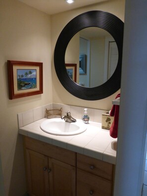 A bathroom with a round mirror, a sink, and a framed picture on the wall.