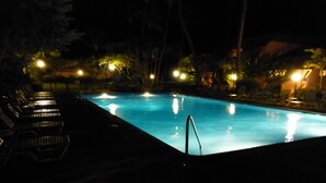 Piscina à noite com espreguiçadeiras e iluminação ambiente.